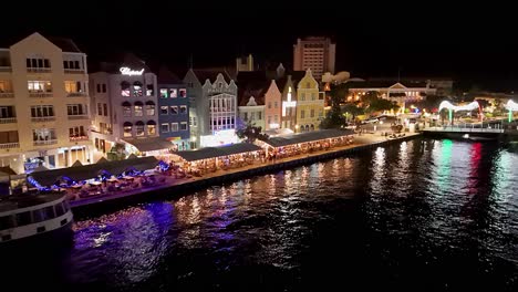 Aerial-pullback-from-waterfront-promenade-of-Willemstad-Curacao-with-ferry-at-night