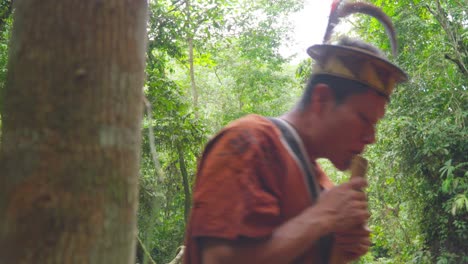 Man-in-traditional-hat-playing-flute-in-lush-Peruvian-jungle,-close-up