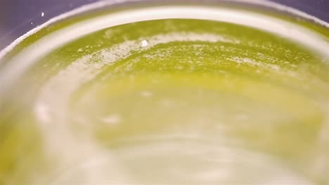 Top-down-view-of-viscous-yellow-liquid-spinning-along-curved-rim-edge-of-glass,-slow-motion