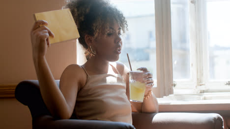 Fashionable-african-woman-drinking-lemonade-fanning-herself-with-a-book
