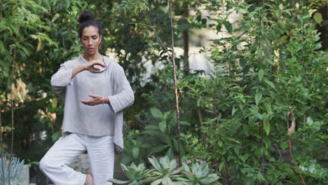 Focused-biracial-woman-practicing-yoga-in-sunny-garden,-slow-motion-with-copy-space