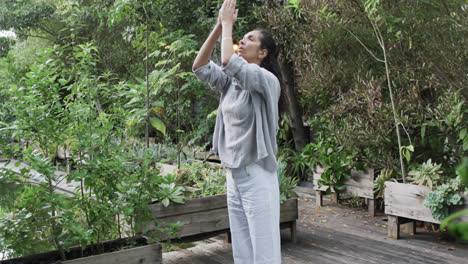 Mujer-Birracial-Enfocada-Practicando-Yoga-En-Un-Jardín-Soleado,-Cámara-Lenta