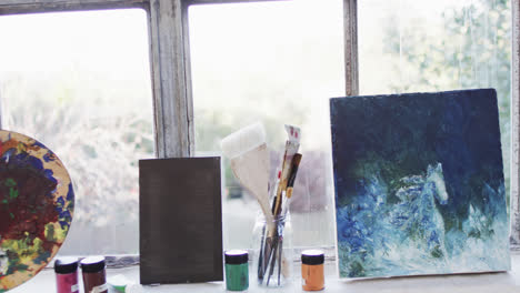 Close-up-of-paintings,-paints-and-brushes-in-studio,-slow-motion