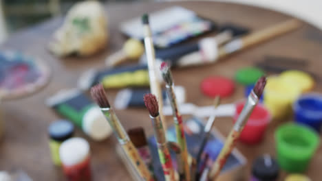Close-up-of-paints-and-brushes-on-table-in-studio,-slow-motion