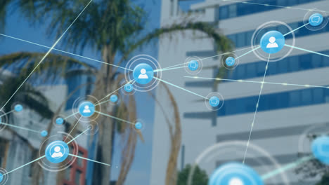 Animation-of-network-of-digital-icons-against-view-of-tall-building-and-palm-tree
