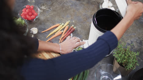 Biracial-woman-composting-waste-of-vegetables-in-kitchen,-slow-motion