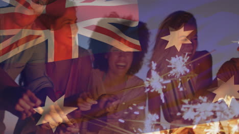 Zusammengesetztes-Video-Der-Australischen-Flagge-über-Einer-Gruppe-Verschiedener-Freunde,-Die-Mit-Wunderkerzen-Am-Strand-Feiern