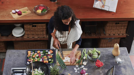 Mujer-Birracial-Cortando-Verduras-Usando-Tableta-En-La-Cocina,-Cámara-Lenta