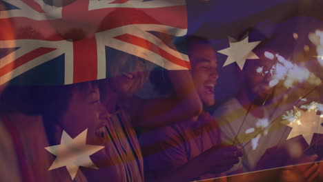 Zusammengesetztes-Video-Der-Australischen-Flagge-über-Einer-Gruppe-Verschiedener-Freunde,-Die-Mit-Wunderkerzen-Am-Strand-Feiern