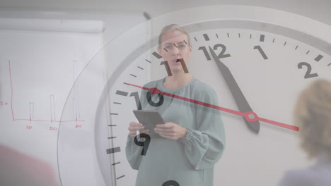 Animation-of-ticking-clock-against-caucasian-woman-holding-a-tablet-giving-a-presentation-at-office