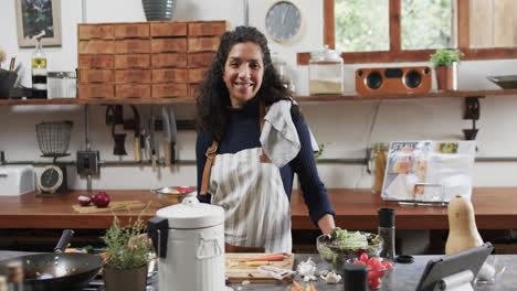 Portrait-of-happy-biracial-woman-in-apron-in-kitchen,-slow-motion