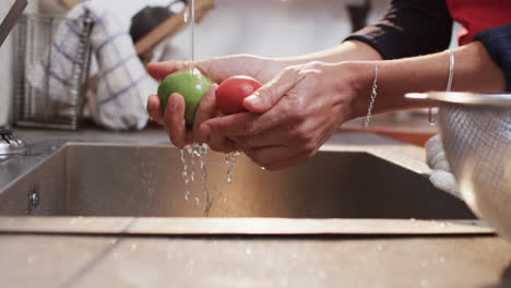 Hands-of-biracial-woman-rinsing-vegetables-in-kitchen,-slow-motion