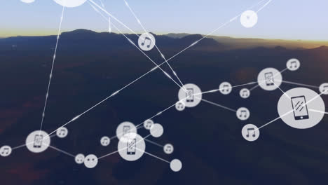 Animation-of-network-of-digital-icons-against-aerial-view-of-mountains-against-sunset-sky