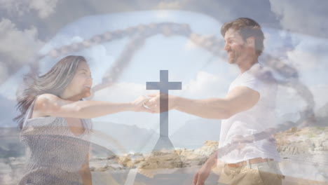 Animation-of-cross-on-mountain,-rosary-on-bible-over-caucasian-couple-dancing-on-beach