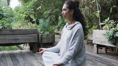 Mujer-Birracial-Enfocada-Practicando-Meditación-De-Yoga-En-Un-Jardín-Soleado,-Cámara-Lenta