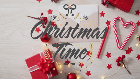 Animation-of-christmas-time-text-over-christmas-decorations,-gifts,-candlies-on-table