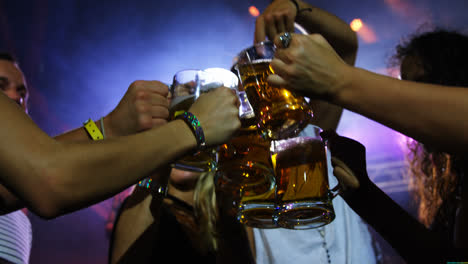 Group-of-friends-toasting-beer-mugs-at-a-concert-4k