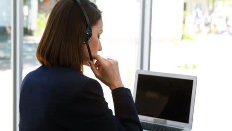 Businesswoman-talking-through-headset-while-using-laptop-at-desk-4k