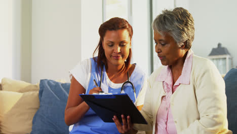 Doctor-explaining-medication-on-clipboard-to-senior-woman-in-living-room-4k