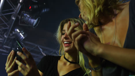 Female-friends-reviewing-pictures-on-mobile-phone-at-a-concert-4k