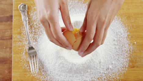 Woman-breaking-eggs-in-the-flour-on-wooden-board-4k