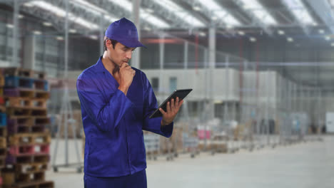 Caucasian-man-worker-wearing-a-blue-overwall-and-a-hat-in-a-factory-using-a-tablet