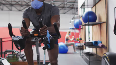 African-american-man-wearing-face-mask-exercising-at-gym