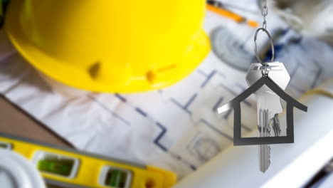 House-keys-and-key-fob-hanging-over-architectural-drawing-and-hard-hat-in-the-background