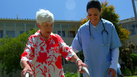 Front-view-of-Caucasian-female-doctor-helping-senior-patient-to-walk-with-walker-in-the-garden-of-nu