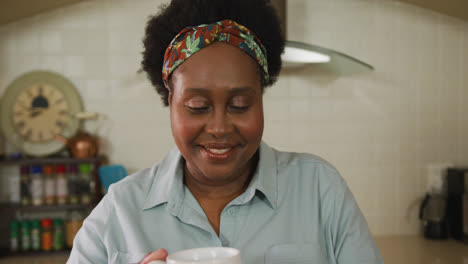 Afroamerikanische-ältere-Frau-Lächelt,-Während-Sie-Zu-Hause-In-Der-Küche-Kaffee-Trinkt