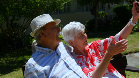 Vorderansicht-Eines-Aktiven-Kaukasischen-älteren-Paares,-Das-Im-Garten-Des-Pflegeheims-Ein-Selfie-Mit-Dem-Mobiltelefon-Macht