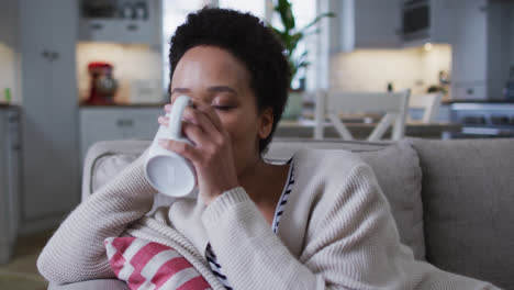 Mixed-race-woman-sitting-on-couch-and-drinking-coffee