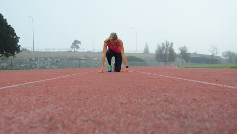 Front-view-of-Caucasian-female-athlete-taking-starting-position-on-running-track-at-sports-venue-4k