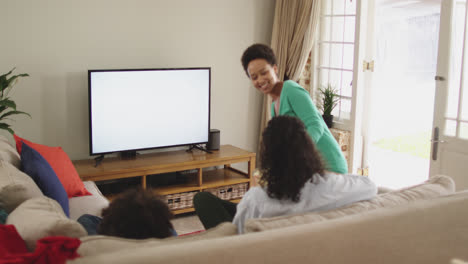 Mixed-race-lesbian-couple-and-daughter-watching-tv-sitting-on-couch