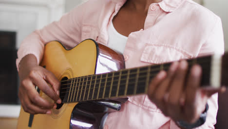 Mid-section-of-african-american-woman-playing-guitar-at-home