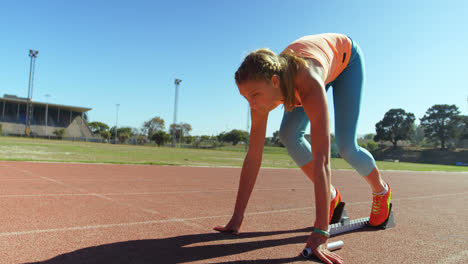 Side-view-of-Caucasian-female-athlete-taking-starting-position-and-running-on-a-running-track-at-spo