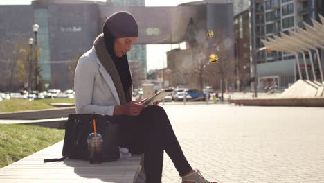 Animation-of-mixed-race-woman-wearing-hijab-in-street-using-tablet-computer-with-floating-emoji