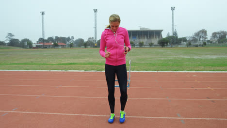 Front-view-of-Caucasian-female-athlete-listening-music-on-mobile-phone-while-exercising-on-race-trac