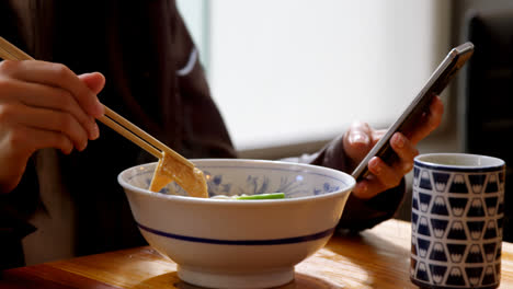Woman-having-noodles-while-using-mobile-phone-in-restaurant-4k