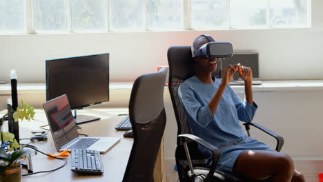 Vista-Frontal-De-Una-Joven-Empresaria-Negra-Sentada-En-El-Escritorio-Y-Usando-Auriculares-De-Realidad-Virtual-4k
