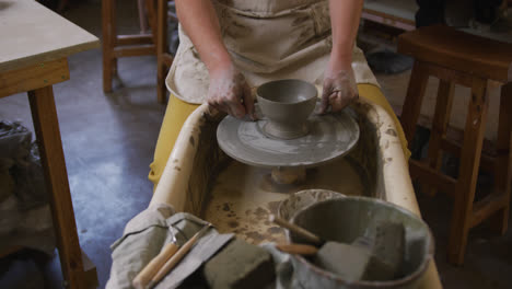 Mid-section-of-female-potter-using-loop-tool-for-finishing-pottery-at-pottery-studio