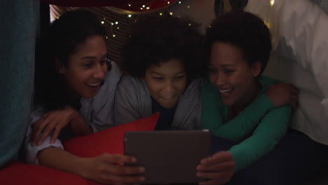 Mixed-race-lesbian-couple-and-daughter-using-tablet-lying-in-bedroom-camp