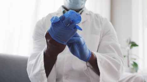Mid-section-of-male-african-american-doctor-wearing-surgical-gloves-at-home