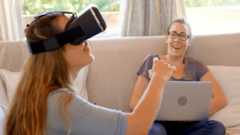 Lesbian-couple-using-virtual-reality-headset-and-laptop-in-living-room-4k