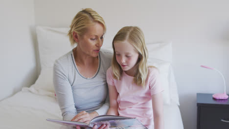 Front-view-of-Caucasian-woman-reading-a-story-to-her-daughter-on-bed