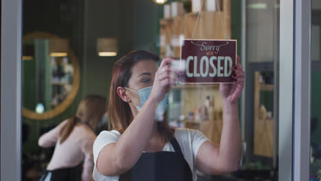 Female-hairdresser-wearing-face-mask-changing-sign-board-from-Closed-to-Open-at-hair-salon