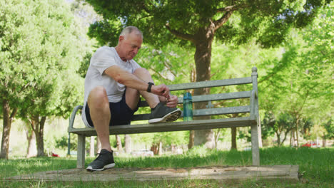 Senior-man-tying-his-shoe-laces-while-sitting-on-a-bench-in-the-park