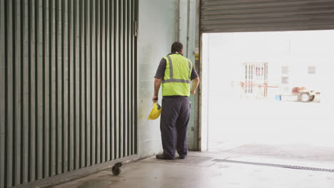 Caucasian-male-factory-worker-at-a-factory--with-a-high-vis-vest,-closing-warehouse-doors
