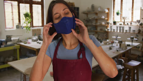 Portrait-of-female-caucasian-potter-wearing-face-mask-at-pottery-studio