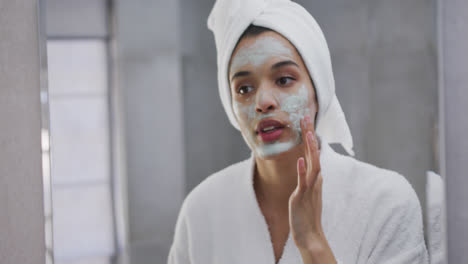 Mixed-race-woman-applying-face-mask-in-bathroom